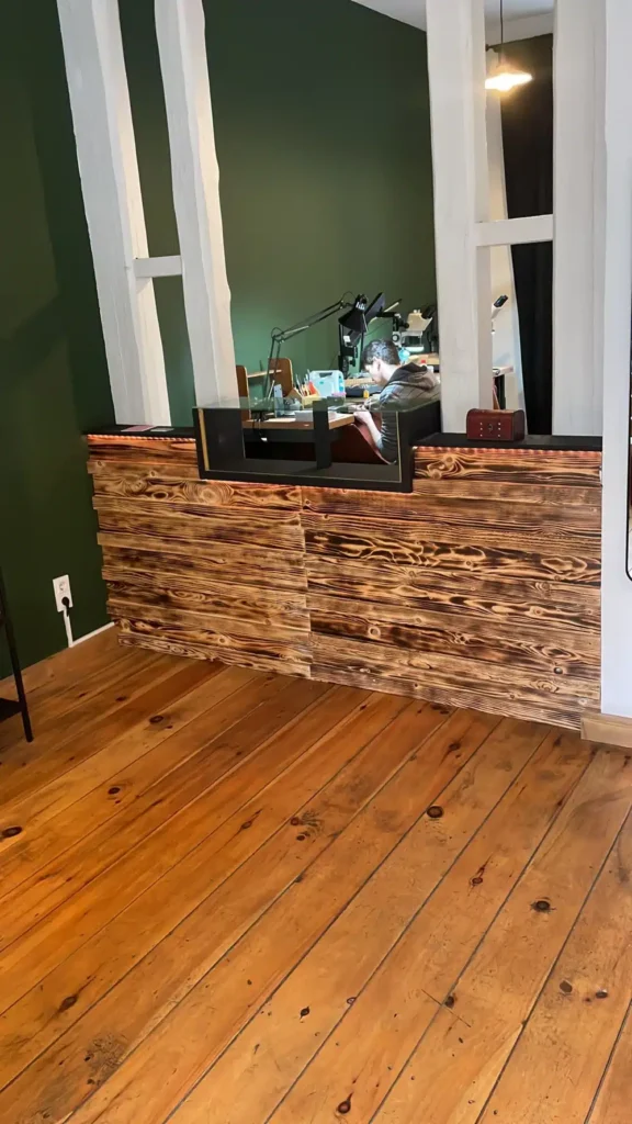 Einblick über eine rustikale Ladentheke aus Holz in einen offenen Werkstattbereich einer Goldschmiede